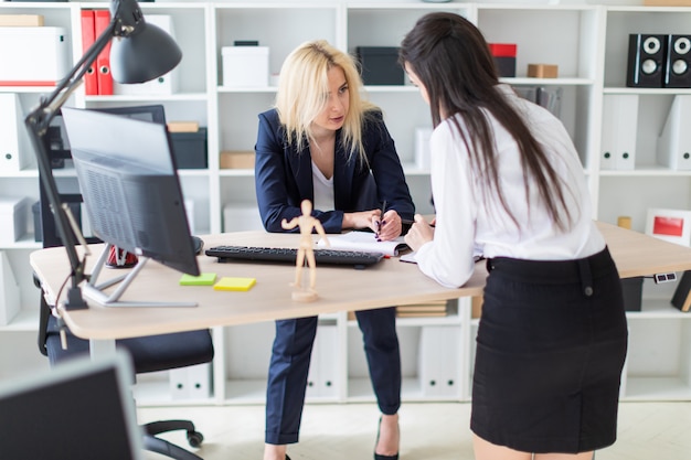 Two Girls Stand In The Office Bent Over Near The Table And Work