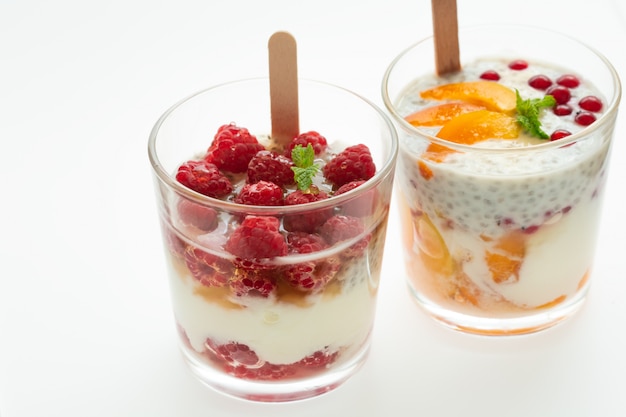 Premium Photo | Two glass of parfait made from greek yogurt with mixed  raspberry, peach, red currant, cherry and chia on a white . healthy  desserts .