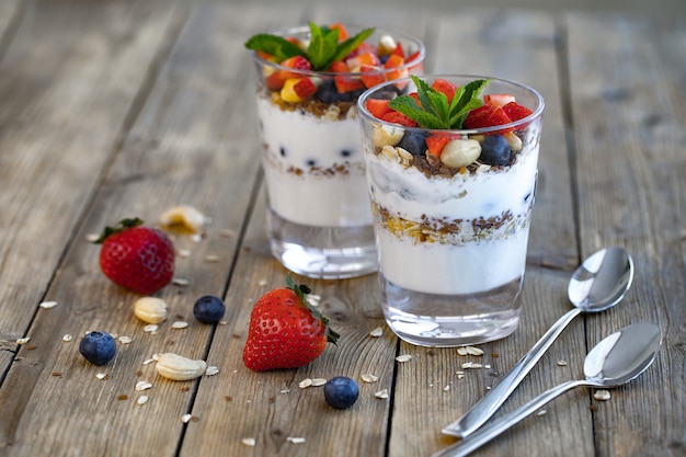 Two glasses of strawberry parfait made from fresh fruit, yogurt, blueberries, flax seeds and muesli on a wooden background. Premium Photo
