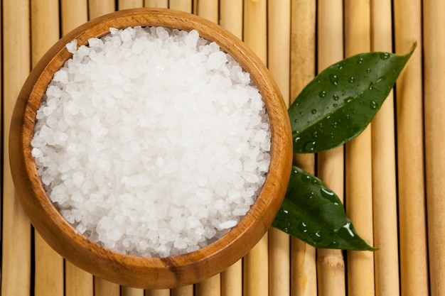 Two green leaves and sea salt in wooden bowl Free Photo