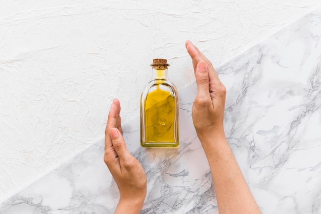 Two hands covering the olive oil bottle on two vivid backdrop Free Photo