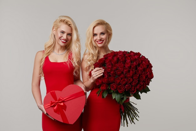 Premium Photo Two Happy Young Twin Women With A Big Bouquet Of Red Roses And A Red Heart Shaped Box