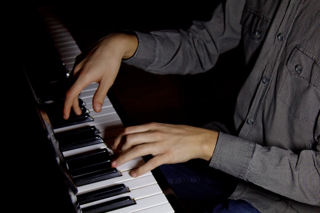 プレミアム写真 ピアノの2つの男性の手 手のひらはキーの上に横になり 音楽学校で鍵盤楽器を演奏します 生徒は遊ぶことを学びます 手 ピアニスト 黒暗い背景