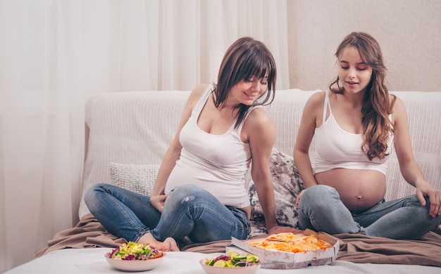 自宅でピザとサラダを食べる2人の妊娠中の女性 無料の写真