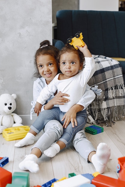 2人のかわいい子供たちが床に座って ソファの近くでおもちゃで遊んでいます 家で遊んでいるアフリカ系アメリカ人の姉妹 プレミアム写真