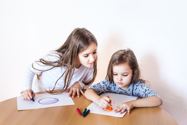 Premium Photo | Two sisters drawing with crayons on paper sheet ...