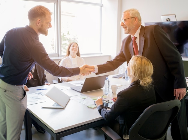 Two smiling businessman shaking hands together in the board meeting Free Photo