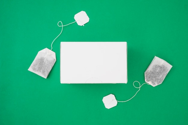 Download Two tea bags on the side of white box over the green background Photo | Free Download