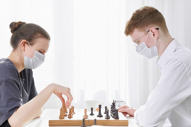 コロナウイルスのパンデミックのため 検疫中に10代の2人がチェスをします 男の子と女の子がボードゲームをプレイ プレミアム写真