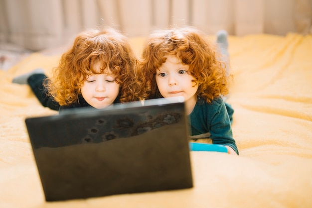 Free Photo | Two twins lying on bed looking at laptop