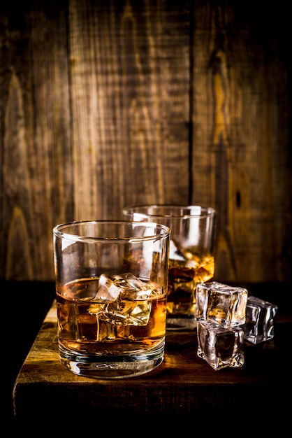 Download Two whiskey shot glasses on dark wooden table, with ice cubes, | Premium Photo