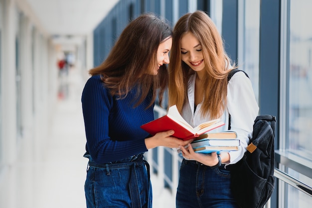Two young female students standing with books and bags in the hallway Premium Photo