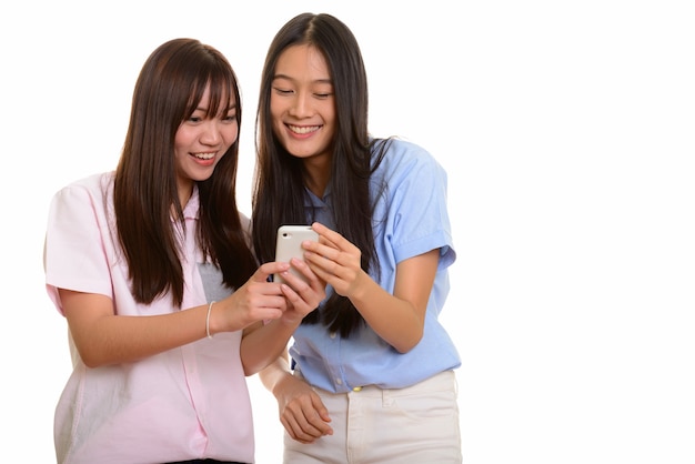 Hai cô gái trẻ châu Á vui vẻ mỉm cười và sử dụng điện thoại di động