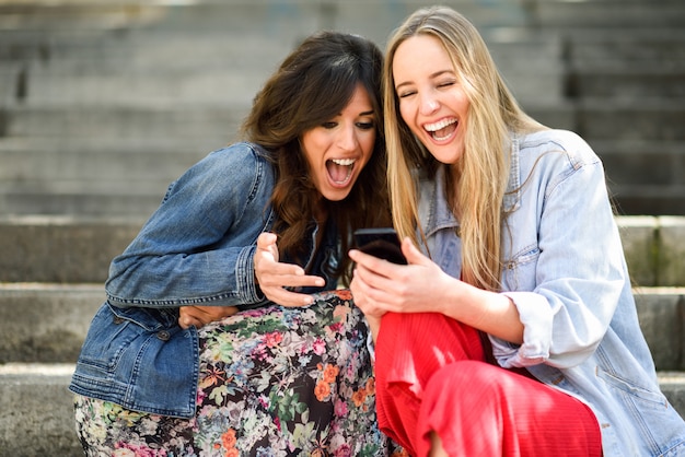 Two young women looking at some funny thing on their smart phone outdoors Free Photo