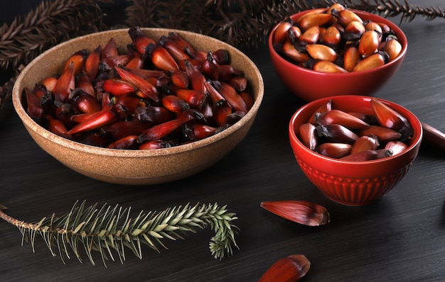 冬にブラジル料理の調味料として使用される典型的なaraucariaの種子 灰色の木製テーブルに茶色と赤の木製ボウルにブラジルのピニオンナッツ プレミアム写真