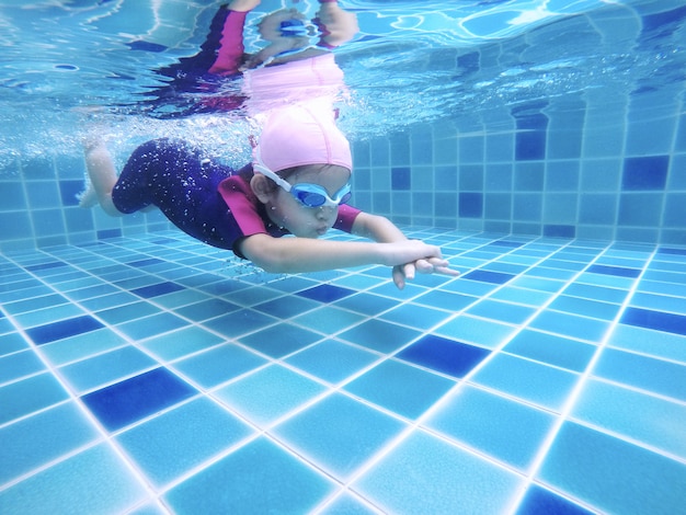 水中の若いかわいい女の子は彼女の水泳の先生と一緒にスイミングプールで泳いでいます プレミアム写真