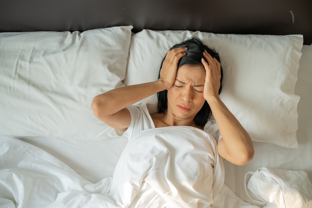 Unhappy exhausted mature woman with closed eyes lying in bed, touching temples close up, tired female suffering from headache or migraine, feeling unwell, suffering from insomnia, lack of sleep Free Photo