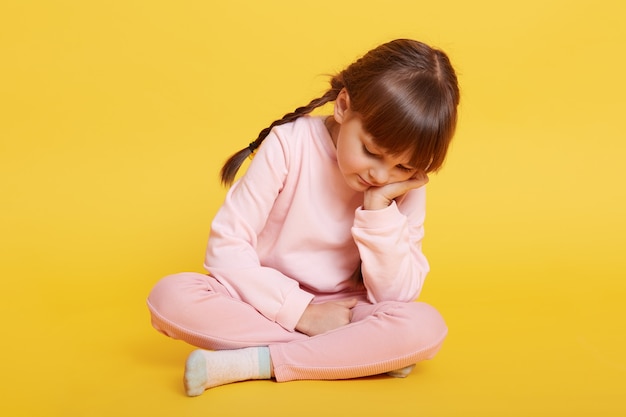 黄色の上に床に座っている不幸な小さな白人の女の子 プレミアム写真