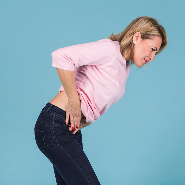 Unhappy woman with abdominal pain standing against blue backdrop | Free ...