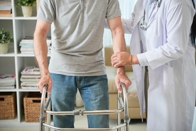 Unrecognizable female doctor helping male patient walk with walking frame Free Photo