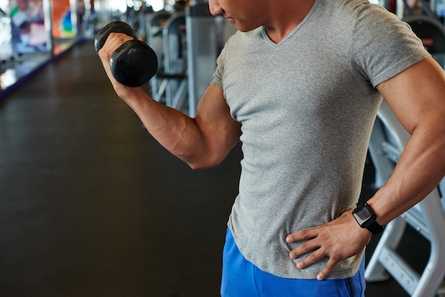 Unrecognizable fit man doing bicep curl with barbell in gym Free Photo