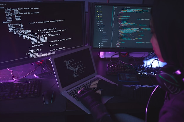 暗い部屋 コピースペースでセキュリティをプログラミングまたはハッキングする複数の画面に囲まれた認識できない若い男 プレミアム写真