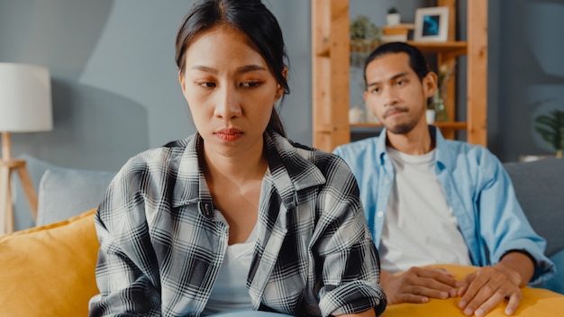 Upset asian couple sit on couch in living room Free Photo