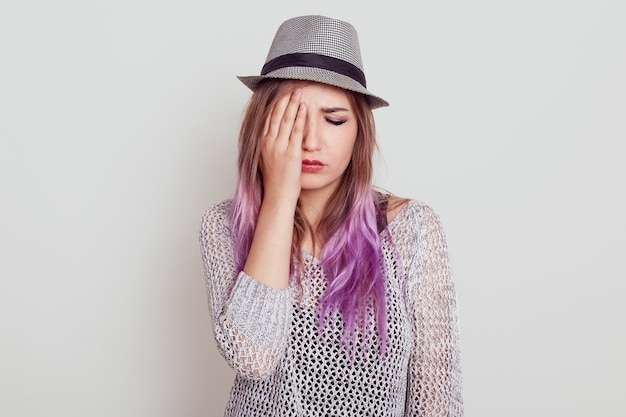 Free Photo Upset Beautiful Woman With Lilac Hair Wearing Shirt And Hat Being Sad Covering Half Of Face With Palm Keeps Eyes Closed Isolated Over White Wall