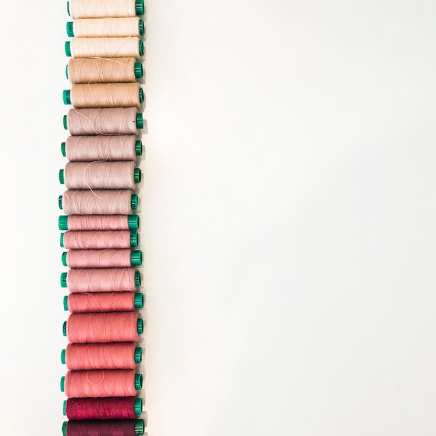Various shade of spools arranged in a row on white backdrop Free Photo
