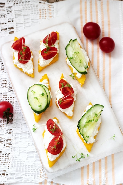 Vegetarian canapes from polenta with cheese, vegetables and cress. rustic style. Premium Photo