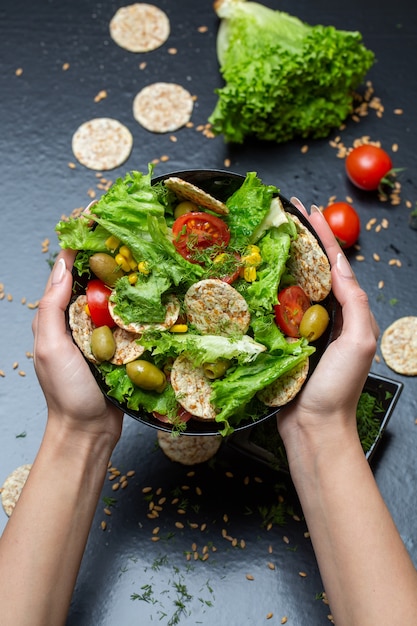 Vertical closeup of a person holding a bowl of salad with crackers and vegetables under the lights Free Photo
