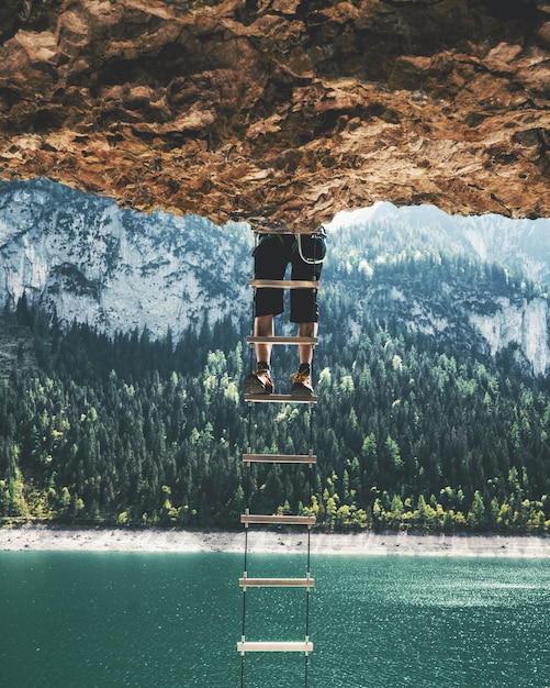 崖からぶら下がっているはしごを登る人の垂直ショット 無料の写真