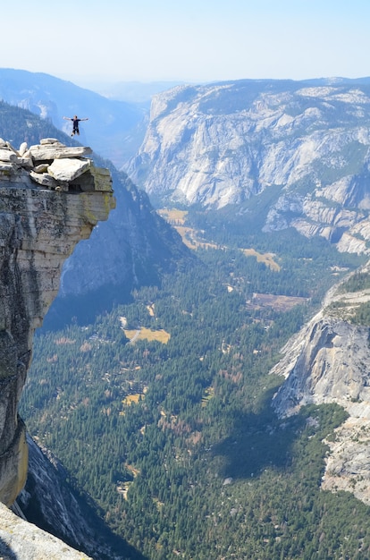 カリフォルニア州ヨセミテのハーフドームで崖の上をジャンプする人の垂直ショット 無料の写真