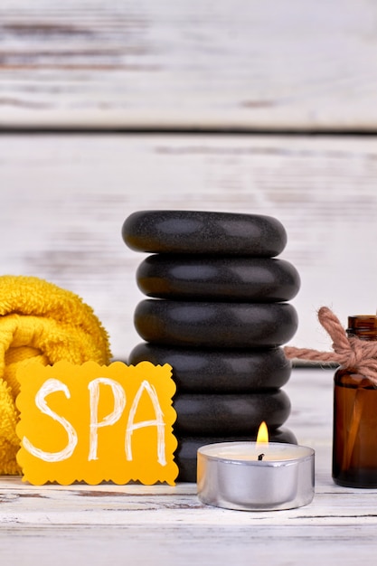 Premium Photo Vertical Shot Spa Treatment Accessories On White Wooden Background Stacl Of Black Polished Stones With Candle And Rolled Towel