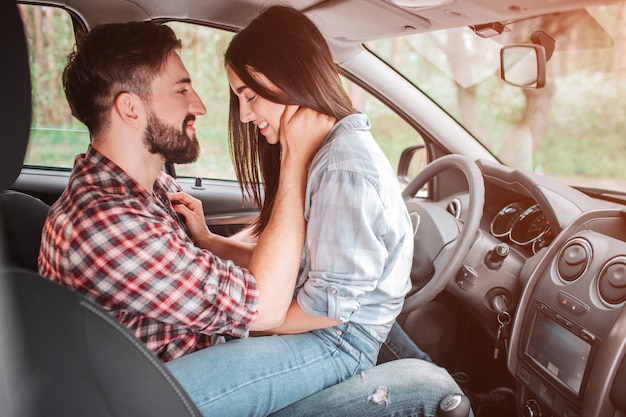 車の中で向かい合って座っている若いカップルの非常に柔らかい写真 彼は彼女の胸に手をつないで下を見下ろしている間 彼は彼女の首に手をつないで女の子を見ています プレミアム写真