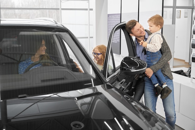 Premium Photo | View from side of happy family looking at new black car ...