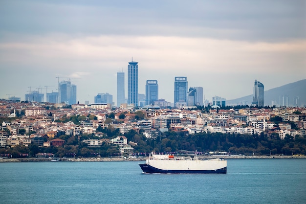 イスタンブール ボスポラス海峡 前景に移動する船 トルコの住宅と高度な近代的な建物のある地区のビュー プレミアム写真