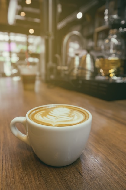 ラテアートコーヒーのヴィンテージトーンカップ ぼかしカフェの背景と木製のテーブルにカプチーノのコーヒー プレミアム写真