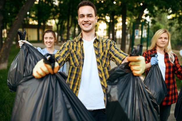 Volunteers holds full plastic trash bags in park, volunteering. male person cleans forest, ecological restoration, eco lifestyle, garbage collection and recycling, ecology care, environment cleaning Premium Photo