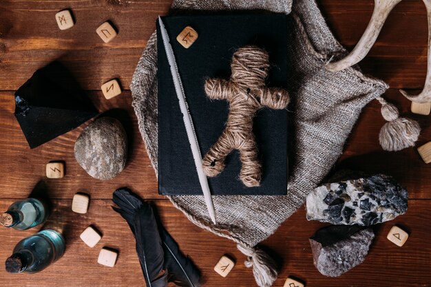 ロープでできたブードゥー教の人形が黒い本の上にあり 魔法の儀式オブジェクトに囲まれています プレミアム写真