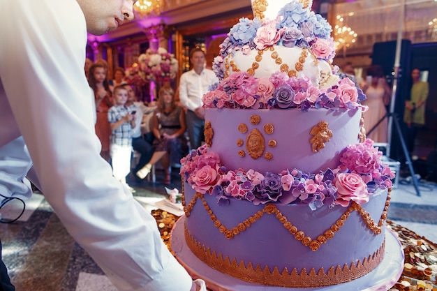 ウェイターは装飾された豪華な紫のウェディングケーキを運びます 無料の写真