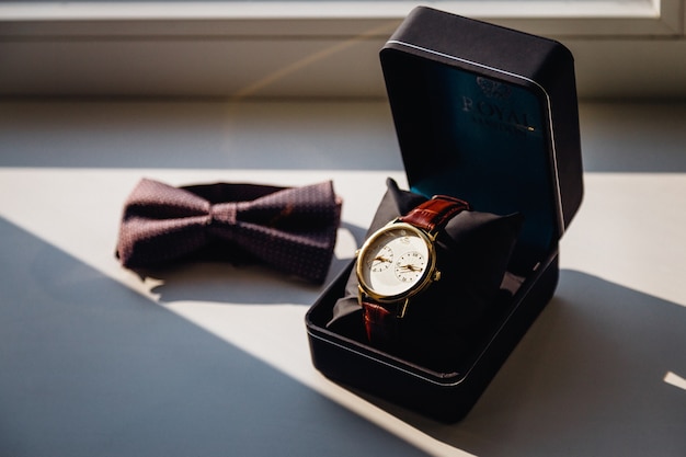 Watch in black box and a bow tie lie on the white windowsill Free Photo