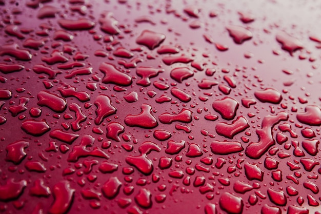 きれいな赤い車に水滴 抽象的な赤背景をぼかし 濡れた表面を持つ車の屋根 プレミアム写真