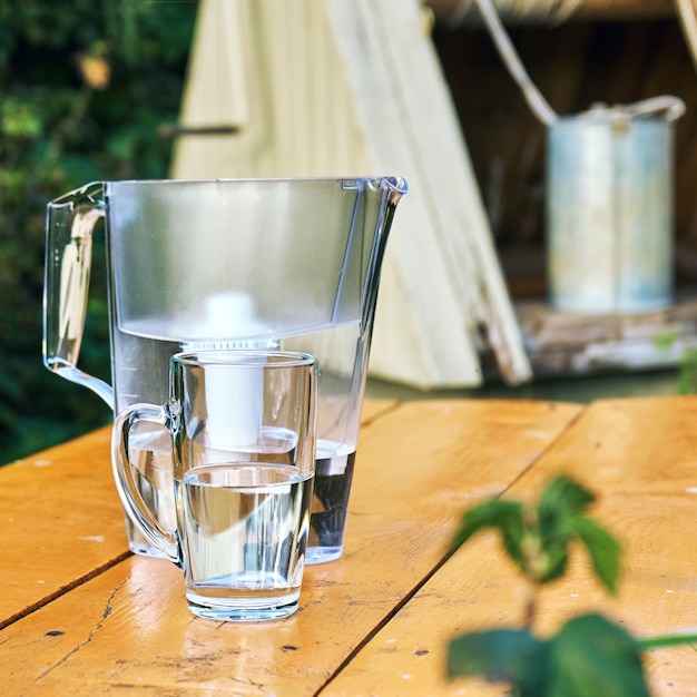 Premium Photo Water Filter Jug And A Transparent Cup Of Water With A Village Well On The Background