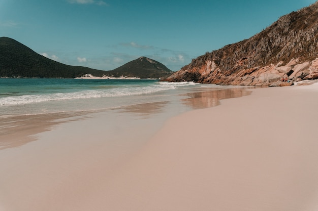 Wavy ocean hitting the sandy beach surrounded by mountains in rio de janeiro Free Photo