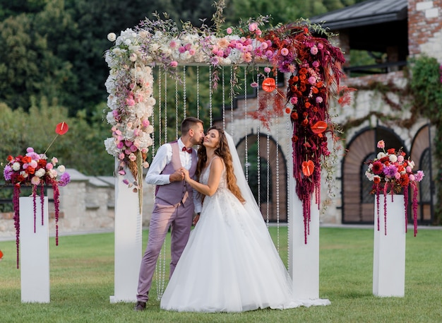 Wedding archway on the backyard and happy wedding couple outdoors before wedding ceremony Free Photo