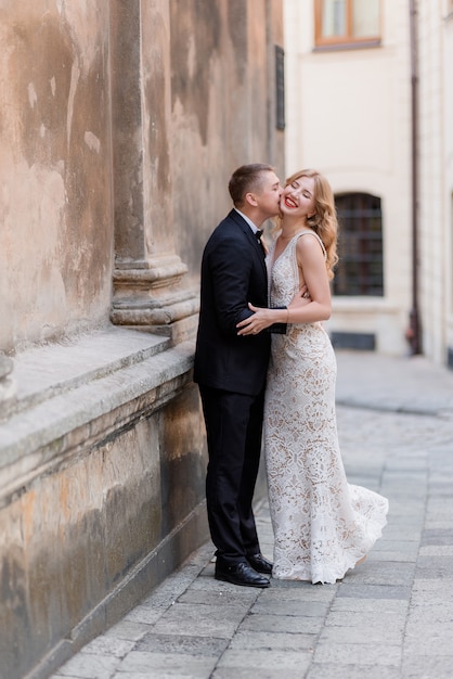 結婚式のカップルは壁の近くの屋外でキス 幸せな笑顔のカップル 狂ったように恋して 無料の写真