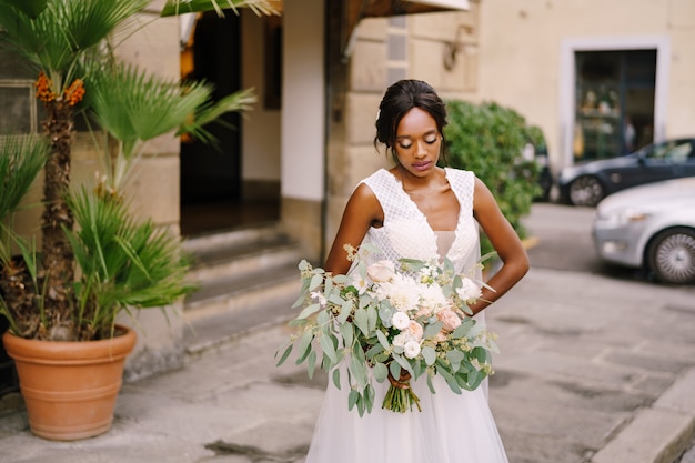 イタリア フィレンツェでの結婚式 白いドレスと長いベールのアフリカ系アメリカ人の花嫁 花嫁の壮大な花束を両腕に プレミアム写真