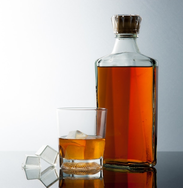 Download Whiskey glass and bottle with ice cubes on gradient background | Premium Photo