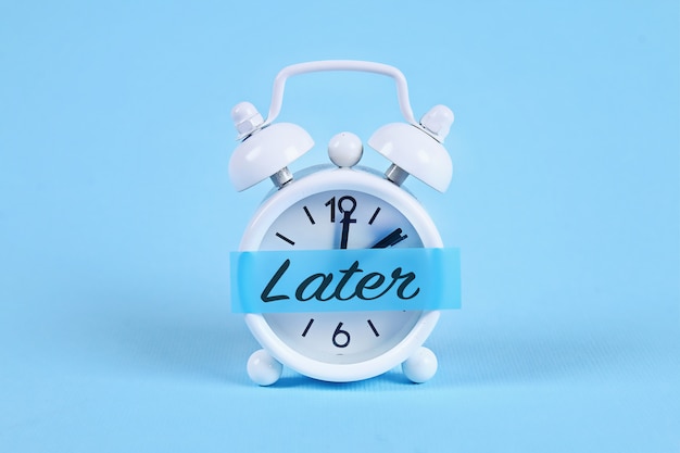 White alarm clock with a sticky note with text later. Premium Photo